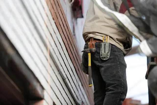 A roofer carrying hand tools across a shingle roof